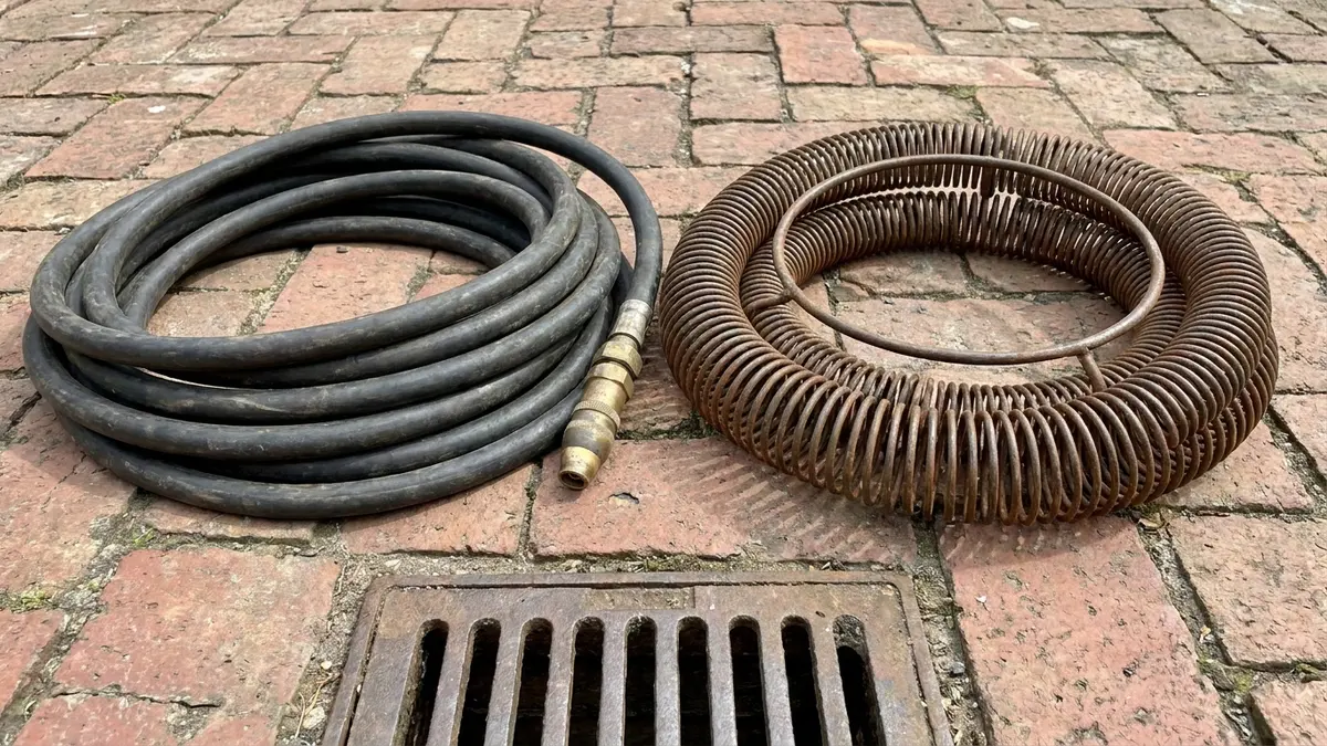 A high-pressure drain jetting hose and a coiled drain snake side by side, drain jetting vs snaking